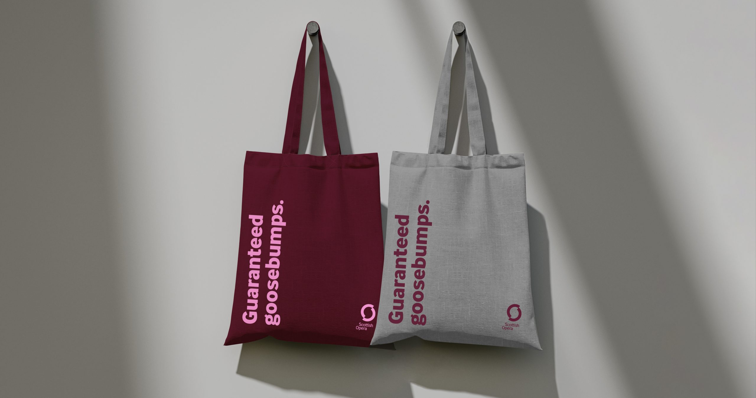 Two Scottish Opera branded tote bags in burgundy and grey, printed with the words 'Guaranteed goosebumps' on them.
