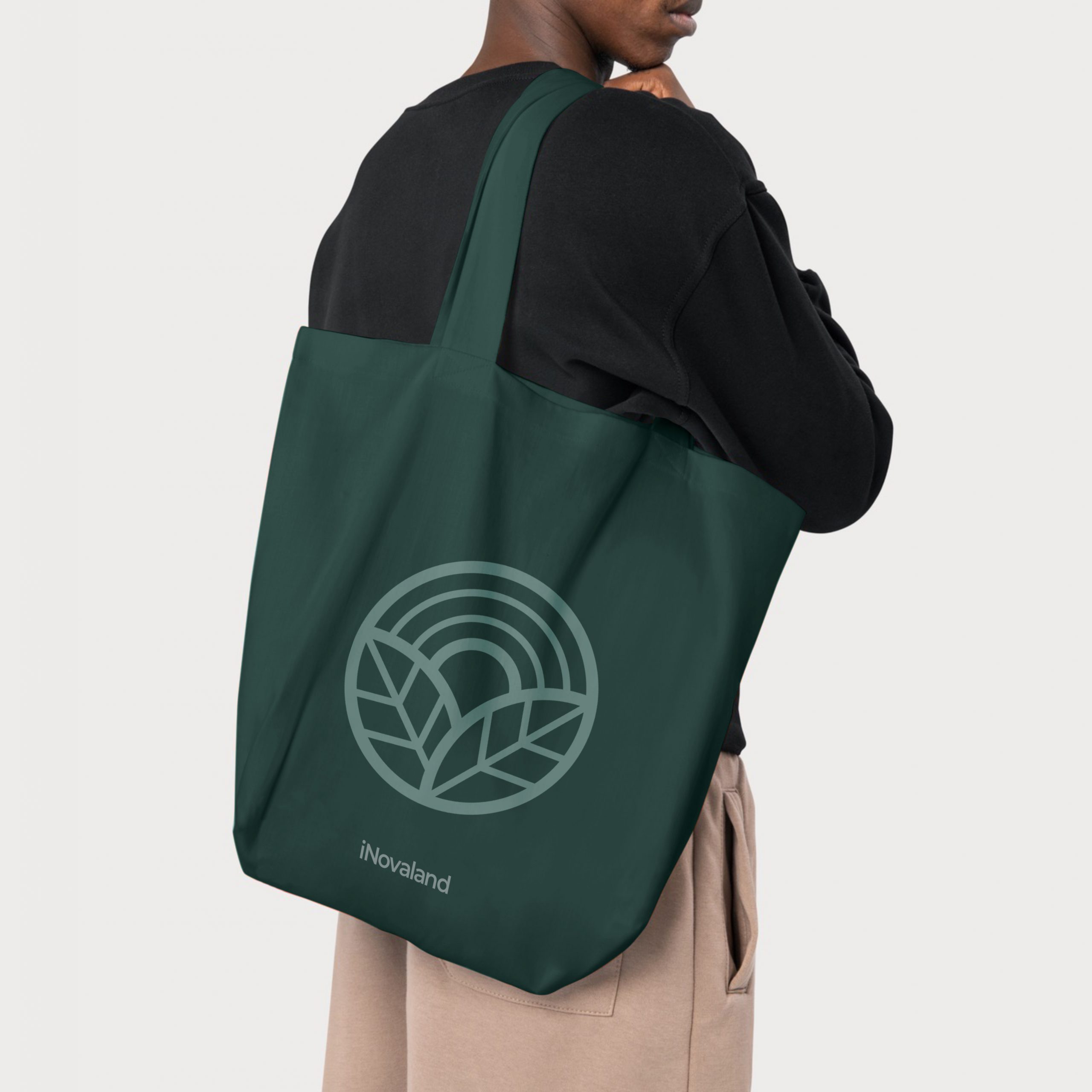 Man carrying a green tote bag with the iNovaland logo printed on the side of it.